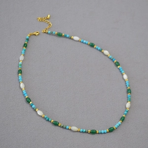 Detail view of turquoise beads and white shell accents on a beaded necklace with gold clasp
