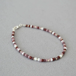 Macro detail of red and gold bohemian seed bead necklace with silver lobster clasp
