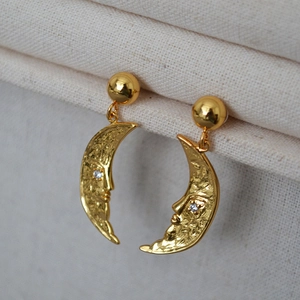 Macro detail of crescent moon earrings with relief texture and a small zircon stud