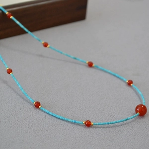 Detail of turquoise tube beads and red agate necklace with gold spacers on stone background