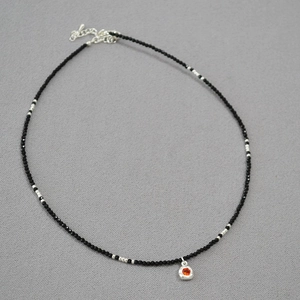 Detail of beaded black spinel necklace with orange gemstone pendant and silver clasp