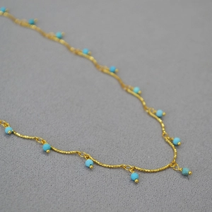 Close-up of gold-plated brass necklace with turquoise beads and twisted rope chain