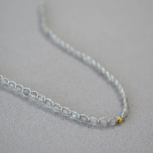 Gros plan de perles en labradorite grise avec une perle dorée sur un cordon tressé