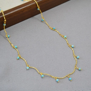 Detail of a thin gold-plated brass necklace featuring faceted turquoise beads on a gray surface