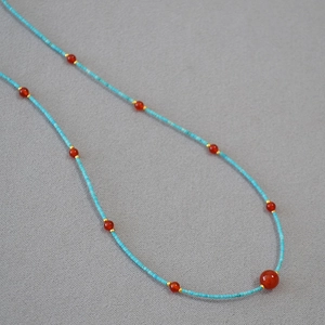 Close-up of handmade turquoise and red agate beaded necklace with gold metal spacers
