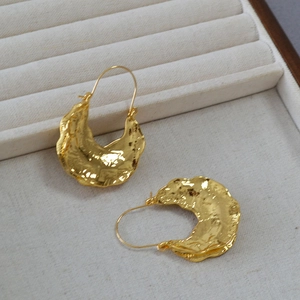 Macro shot of gold-plated fan-shaped earrings with irregular molten lava texture