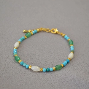 Detailed macro view of beaded bracelet with turquoise and gold accents on gray fabric