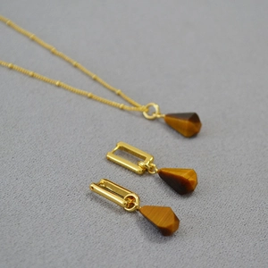 Detailed set of teardrop tiger eye stone necklace and earrings on gray background