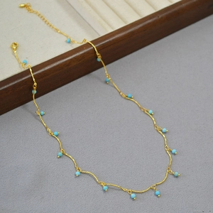 Detailed view of a gold-plated necklace with small turquoise beads and lobster clasp