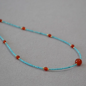 Close-up of turquoise beads and red agate beads with gold accents on a dainty necklace