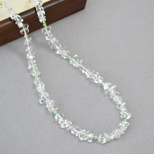 Minimalist clear quartz beaded necklace with turquoise accents on grey fabric background