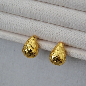 Detailed view of gold plated teardrop earrings with textured faceted scale surface