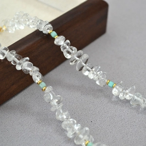 Detail of beaded necklace featuring irregular clear quartz and turquoise accents on wood