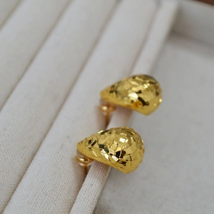 Detail of gold water drop earrings with faceted texture on a beige jewelry display