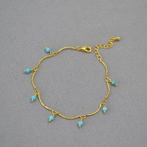 Gold plated beaded necklace with faceted turquoise beads on a textured grey background
