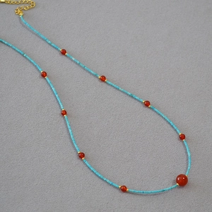 Detail of beaded turquoise necklace with red agate accents and golden metallic clasp