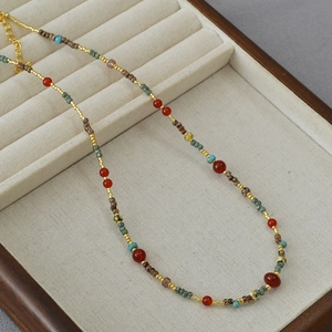 Close-up of red agate and turquoise beads with a golden lobster clasp on a display tray