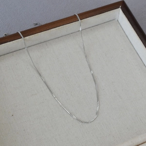 Minimalist silver stainless steel Cuban link necklace displayed on a linen jewelry tray