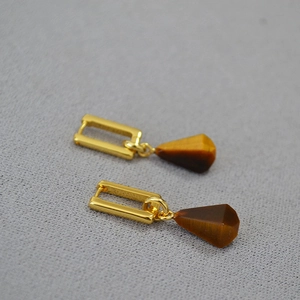 Macro detail of gold plated brass earrings featuring geometric tiger eye stone pendants