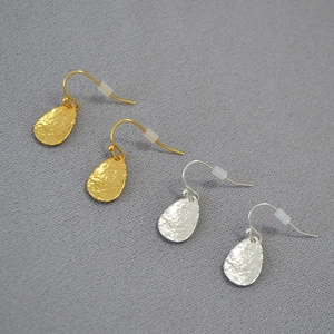 Detail of hammered metal leaf earrings in gold and silver finish on gray fabric