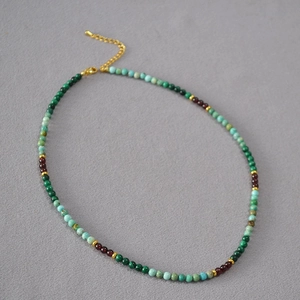 Détail de collier fait main en malachite et grenat sur fond de tissu gris foncé