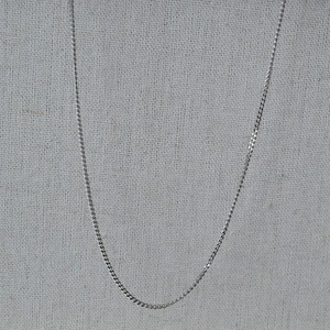 Detailed close-up of a slim silver stainless steel curb chain on a linen fabric background