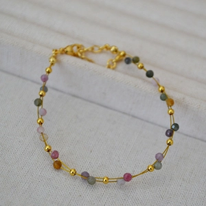 Macro detail of double-layer gold chain bracelet with colorful faceted gemstone beads