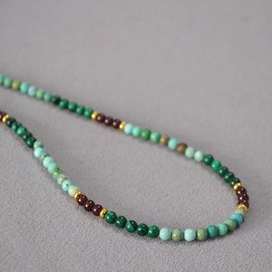 Gros plan de perles de malachite turquoise et grenat avec intercalaires dorés sur tissu