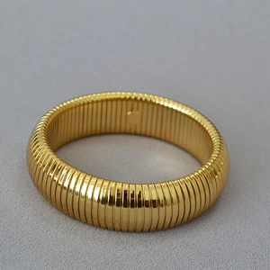 Detailed close-up of wide gold-plated ribbed metal cuff bracelet with high-gloss finish