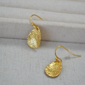 Detail of gold leaf teardrop earrings showing handcrafted hammered texture on a cream fabric