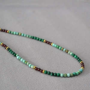 Détail du collier de perles en malachite, turquoise et grenat avec des perles dorées
