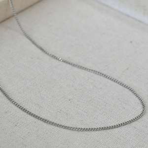 Close-up of a silver stainless steel Cuban link chain necklace on textured fabric