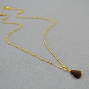 Macro shot of French vintage gold-plated bean chain with a tiger eye stone geometric pendant