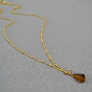 Detailed view of tiger eye stone pendant on a gold beaded chain with geometric cut
