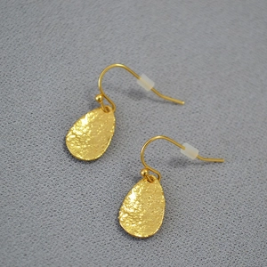 Detail of drop-shaped gold leaf earrings with textured hammered finish and ear hooks