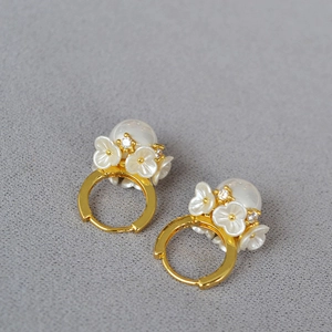 Détail de boucles d'oreilles fleurs dorées avec pétales blancs, perles et zircons