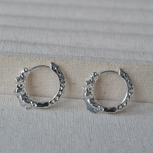 Close-up of silver hoop earrings with hammered texture and blue rhinestones inlay