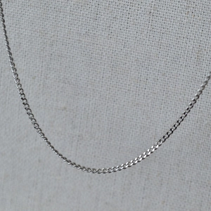 Close-up of a slim silver stainless steel Cuban link chain necklace on grey texture