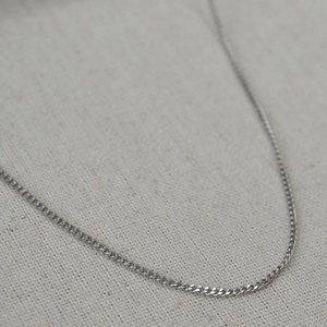 Close-up of minimalist stainless steel curb chain necklace on natural linen background