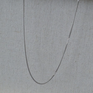Close-up of minimalist silver stainless steel Cuban link necklace on textured cloth