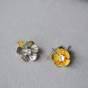 Vue macro des boucles d'oreilles fleur or et argent avec texture martelée et zircon central