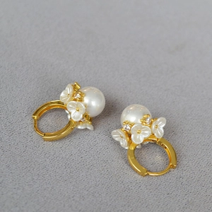 Détail de boucles d'oreilles dorées avec fleurs blanches, zircons et perles pendantes