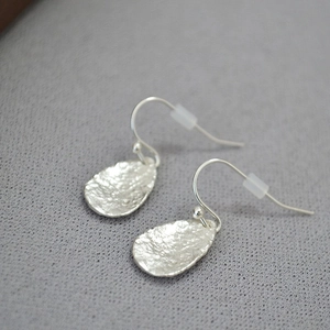 Detailed close-up of silver teardrop leaf earrings with hammered metal texture finish