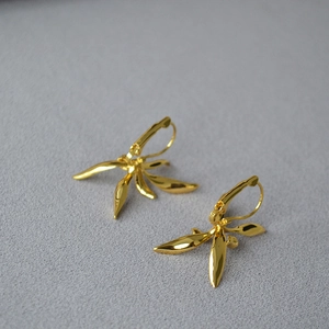 Elegant gold iris flower earrings with irregular petals on a textured violet fabric background