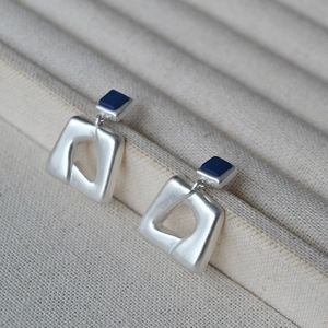 Matte silberne geometrische Ohrhänger mit marineblauen Quadraten auf beigem Tablett