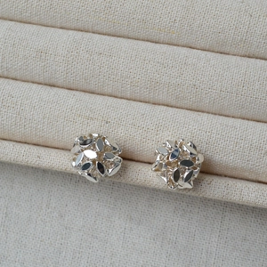 Macro shot of silver multifaceted flower cluster studs on a beige fabric display stand