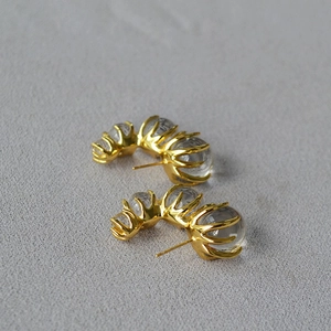 Macro shot of gold C-shaped earrings featuring three transparent glass gradient spheres