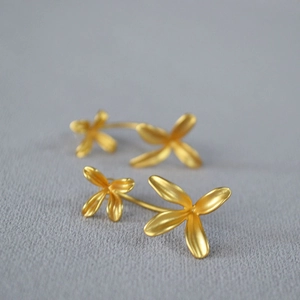 Macro view of golden matte four-petal flower earrings on a grey velvet surface