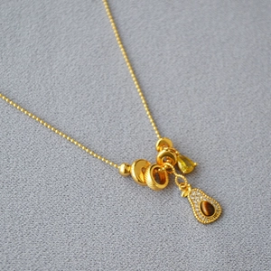 Detail of gold bead chain with tiger eye avocado pendant and teardrop gemstone charm