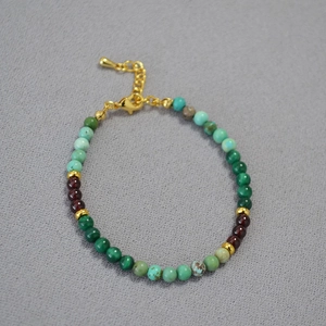 Collier fait main en perles de malachite et grenat sur un fond de tissu gris texturé